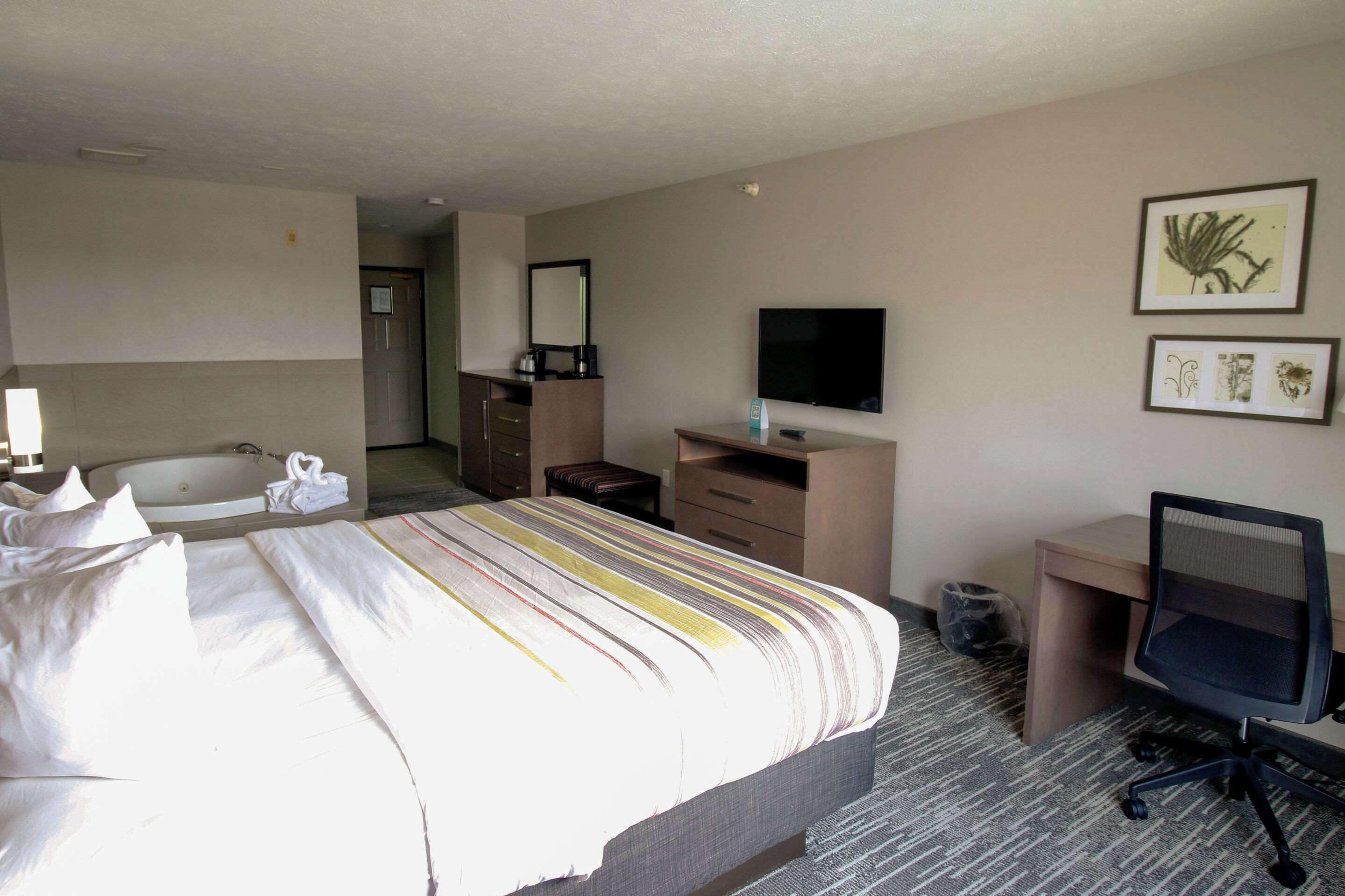 A hotel room with a bed, a desk, a chair, a television, a mirror, and a bathroom with a sink and a bathtub.
