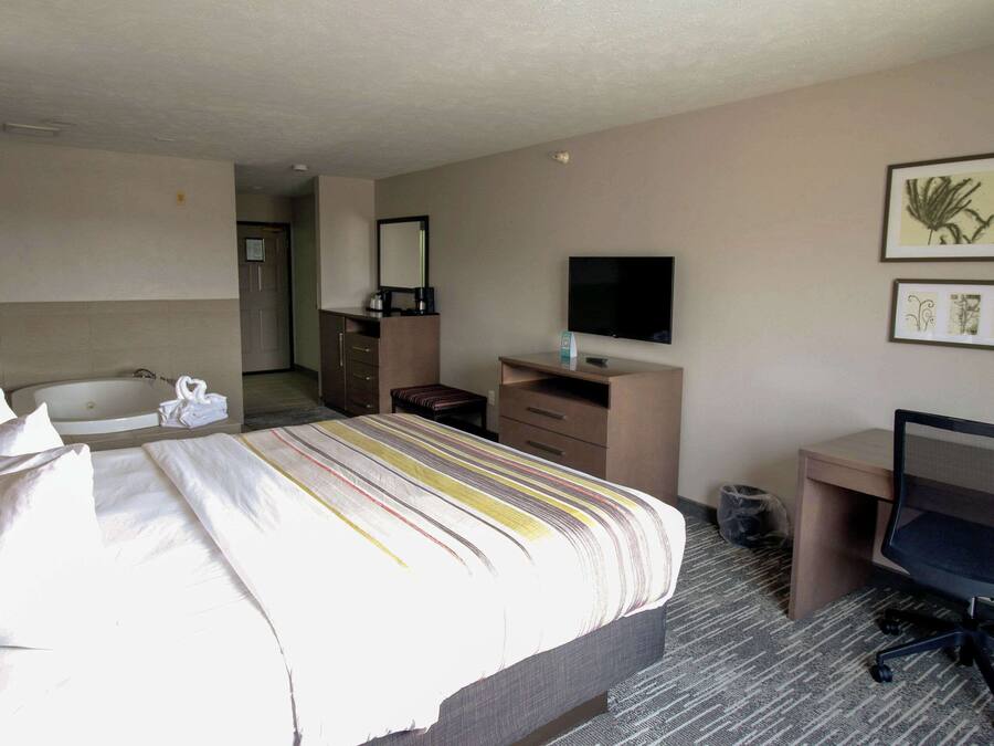 A hotel room with a bed, a desk, a chair, a television, a mirror, and a bathroom with a sink and a bathtub.