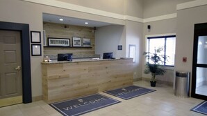 A reception area with a wooden counter, framed pictures, and a welcome mat. - Country Inn & Suites by Radisson, Council Bluffs, IA (Council Bluffs)