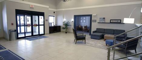 A spacious lobby with a chandelier, a reception desk, a seating area with sofas, and a staircase.