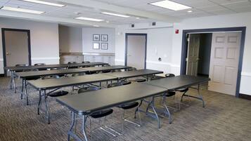 Une salle de conférence dotée de plusieurs tables et chaises, d’un sol recouvert de moquette et de murs blancs.