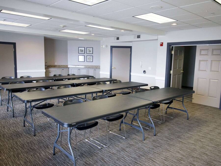 Une salle de conférence dotée de plusieurs tables et chaises, d’un sol recouvert de moquette et de murs blancs.