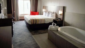 A hotel room with a bed, a red chair, a desk, a bathroom with a bathtub, and a large window with curtains. - Country Inn & Suites by Radisson, Council Bluffs, IA (Council Bluffs)