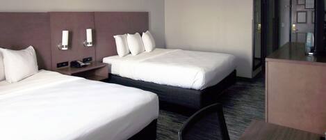 A hotel room with two beds, a desk, and a chair.