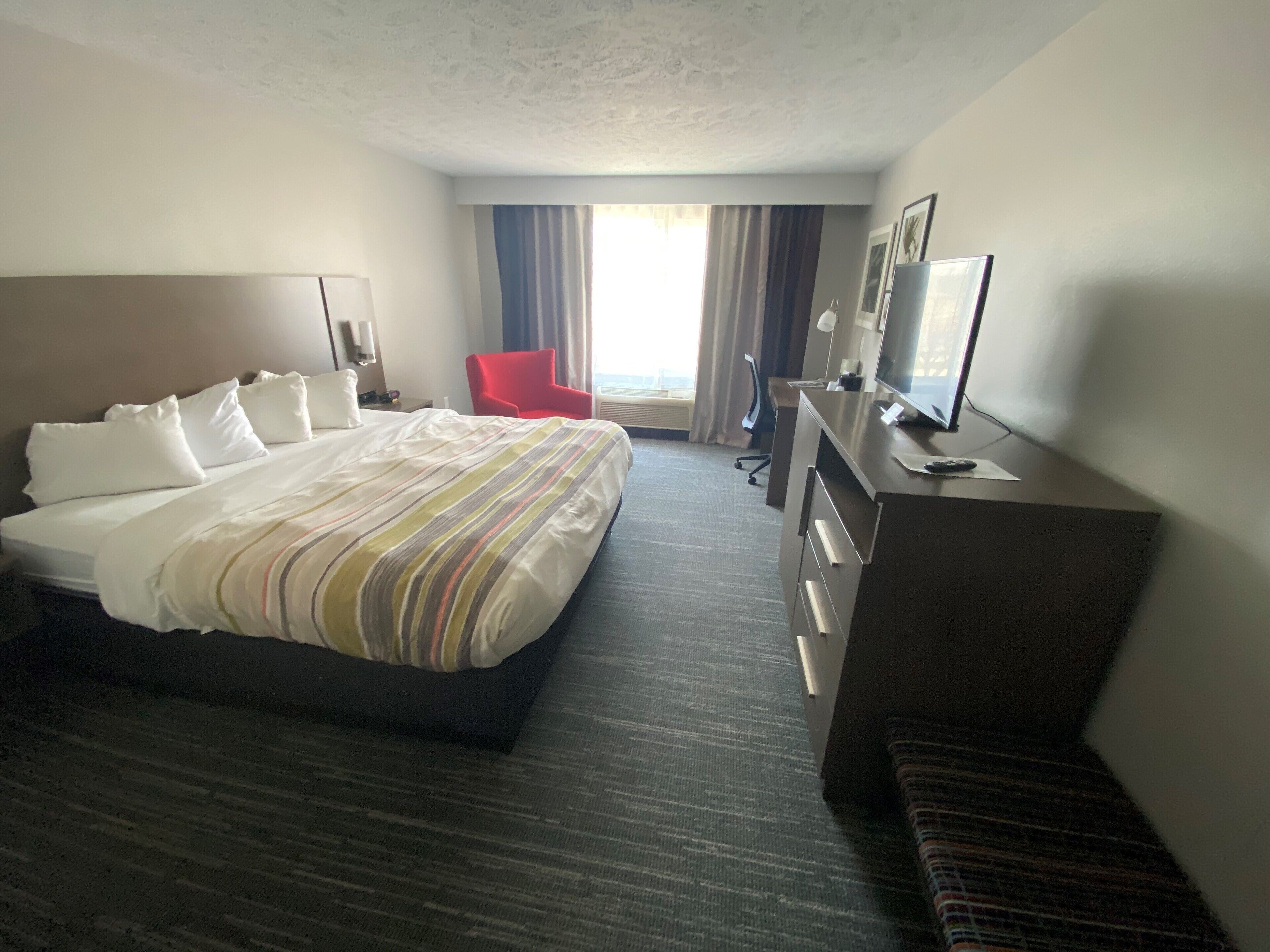 A hotel room with a large bed, a desk with a computer, a red chair, and a window with curtains.