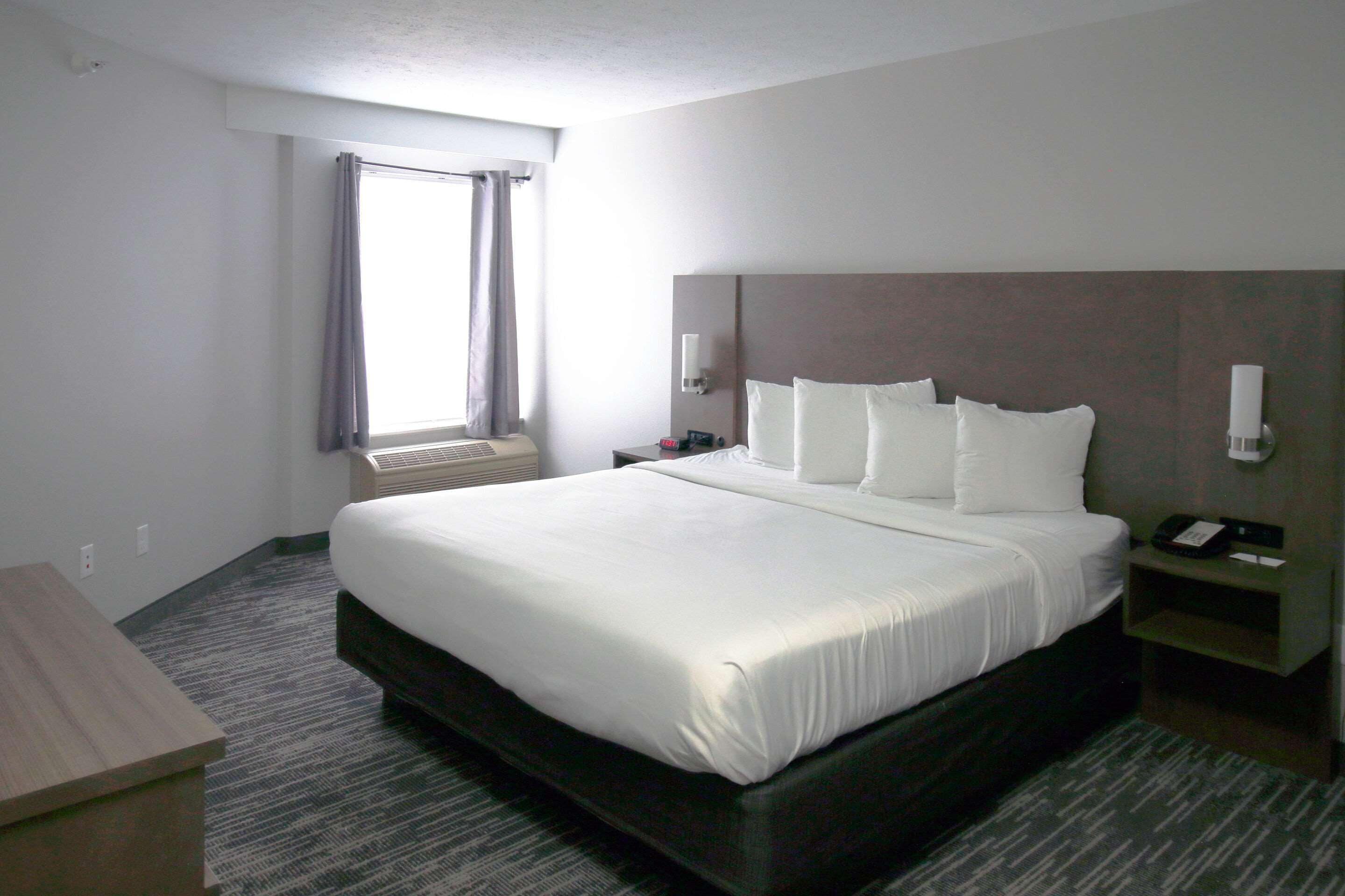 Habitación de hotel con una cama grande, una mesita de noche, una lámpara y una ventana con cortinas.