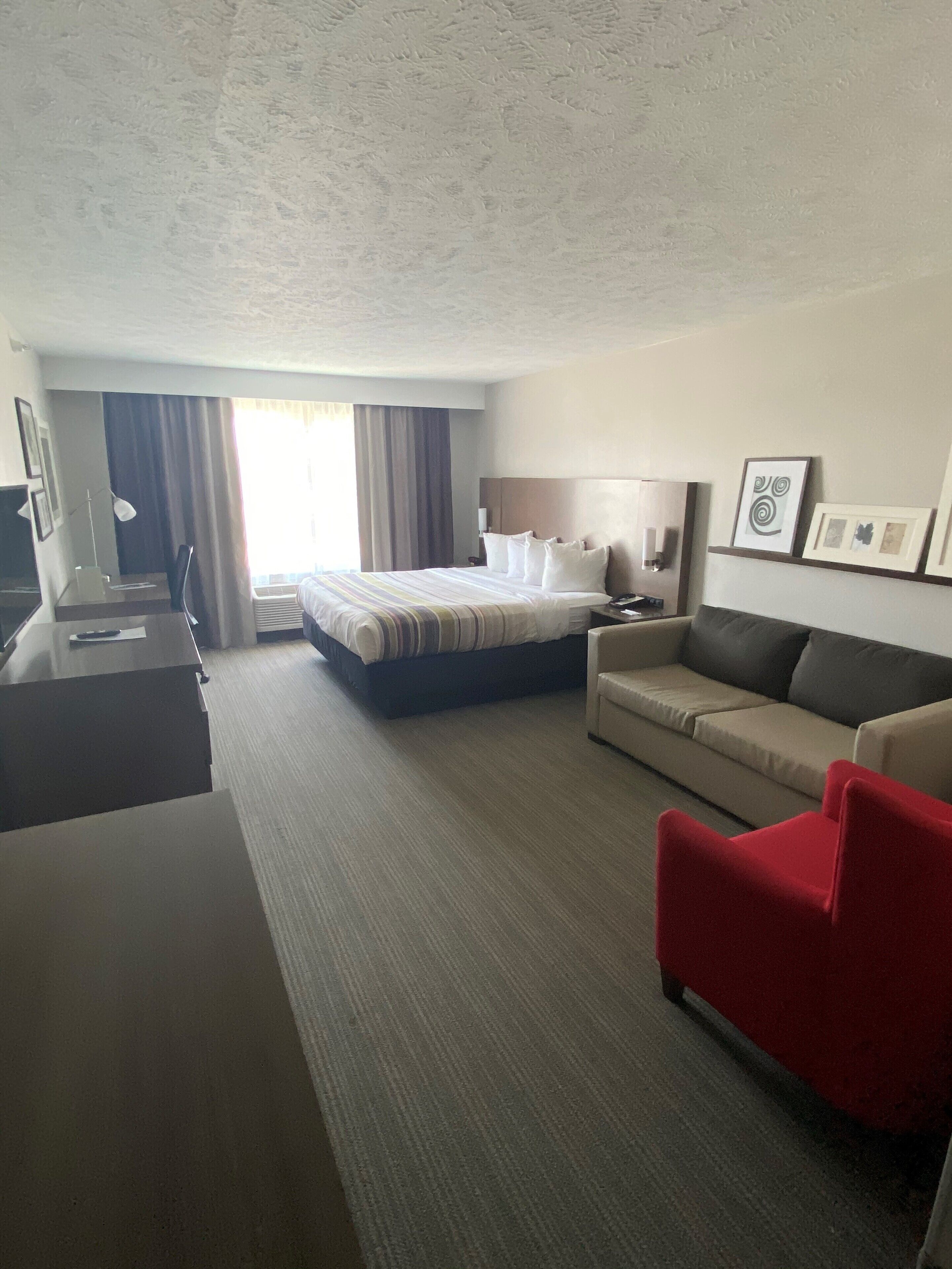 Habitación de hotel con cama, escritorio, sillón rojo, sofá y pared con cuadros.
