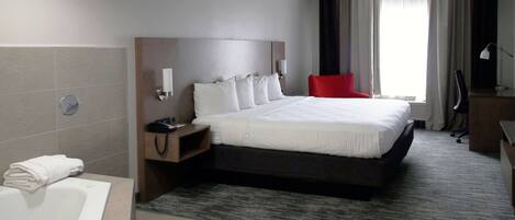 Quarto de hotel com uma cama grande, uma cadeira vermelha, uma escrivaninha com uma lâmpada, um telefone e um banheiro com banheira e toalha.