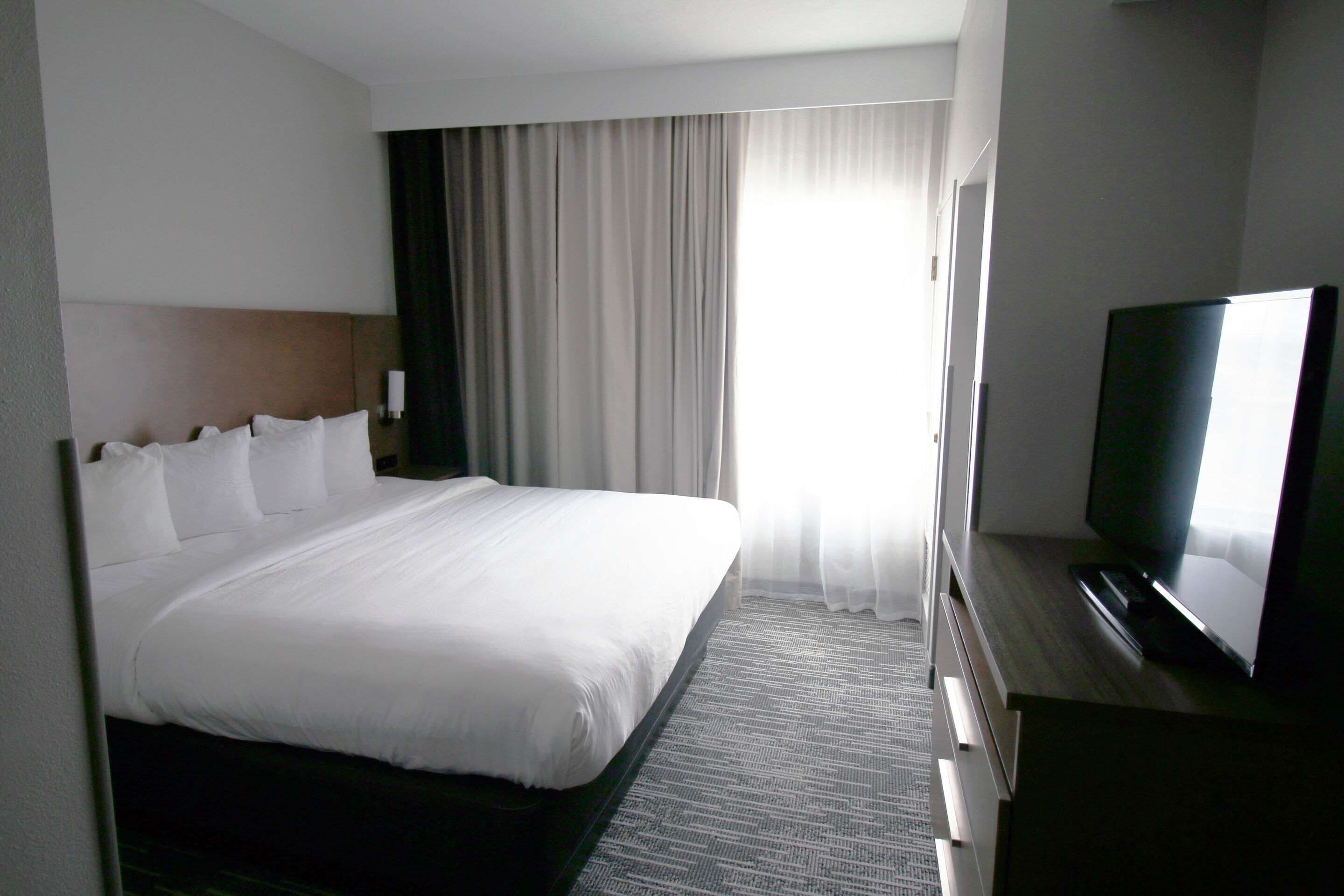 Una habitación de hotel con una cama grande, un televisor de pantalla plana y un ventanal con cortinas.