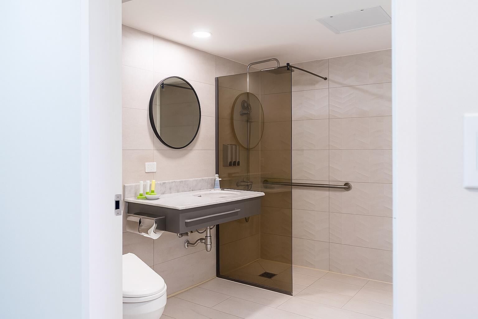 A modern bathroom with a glass-enclosed shower, a round mirror, and a white sink with a towel rack.