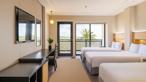 A hotel room with a desk, two beds, a TV, and a balcony with a view. - Bayview Hotel Guam (Tamuning)
