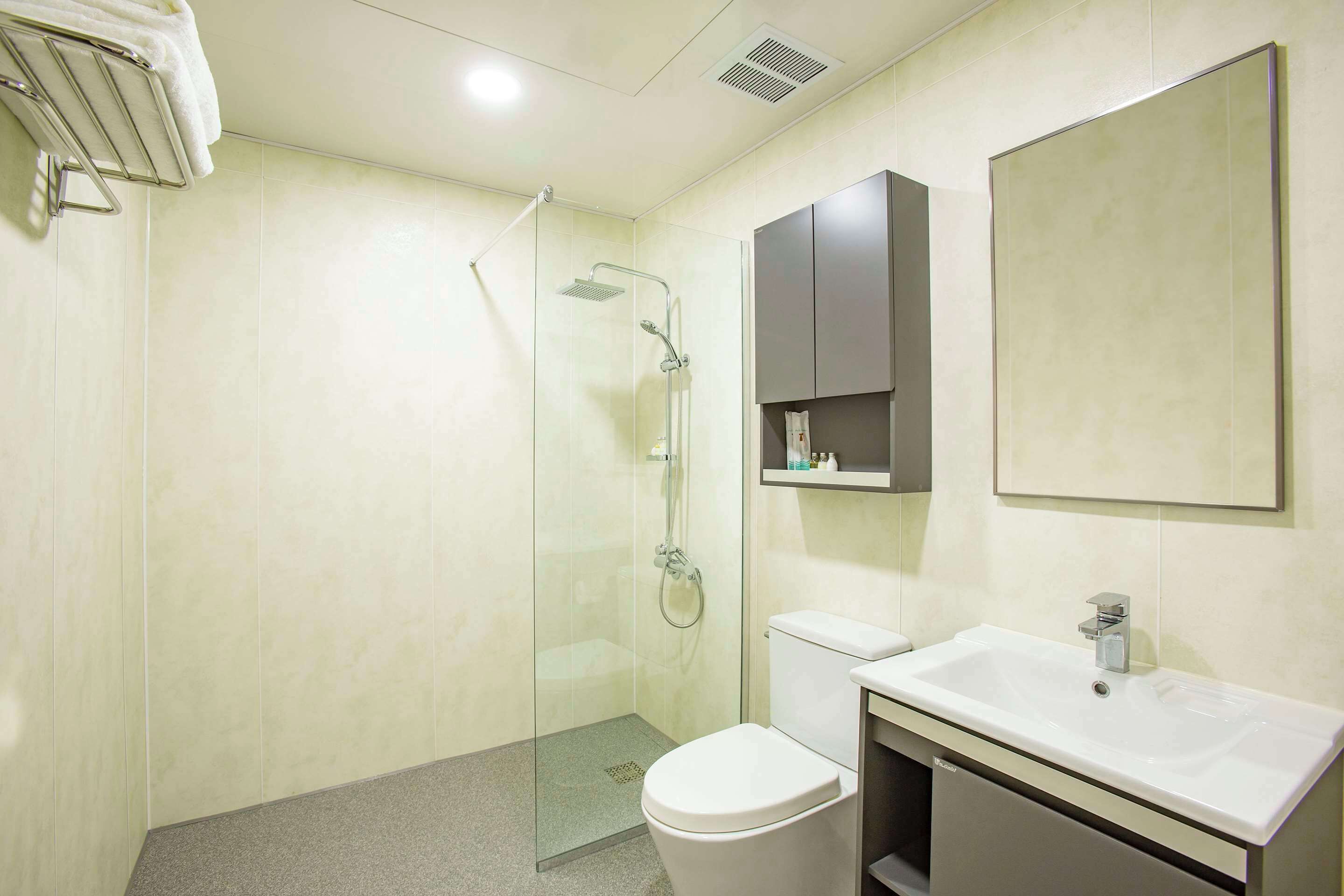 A modern bathroom with a glass-enclosed shower, a white toilet, and a sink with a mirror above it.