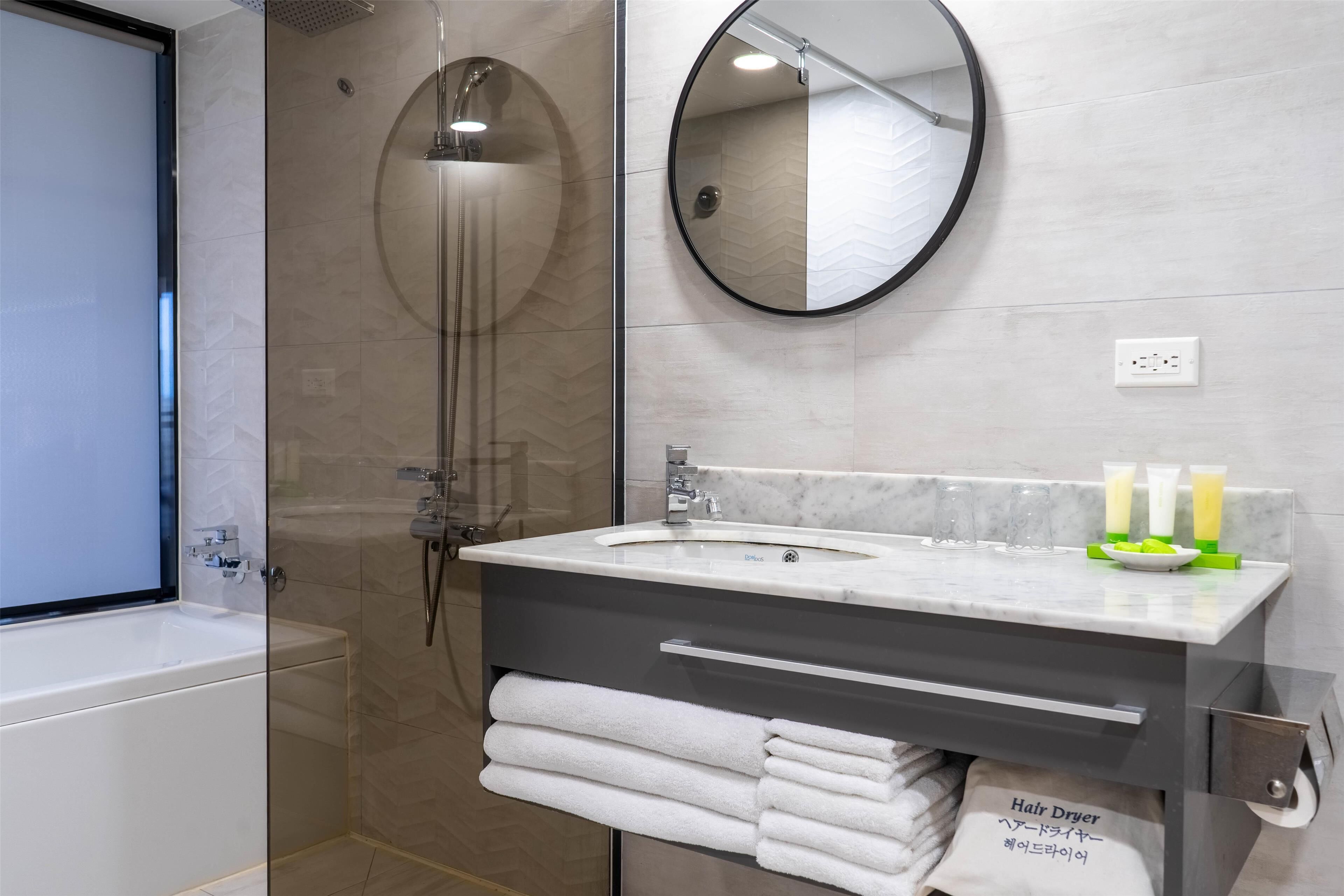 Un bagno moderno con doccia vetrata, specchio rotondo, lavabo in marmo e asciugamani piegati con cura.
