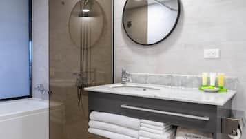 Un bagno moderno con doccia vetrata, specchio rotondo, lavabo in marmo e asciugamani piegati con cura.