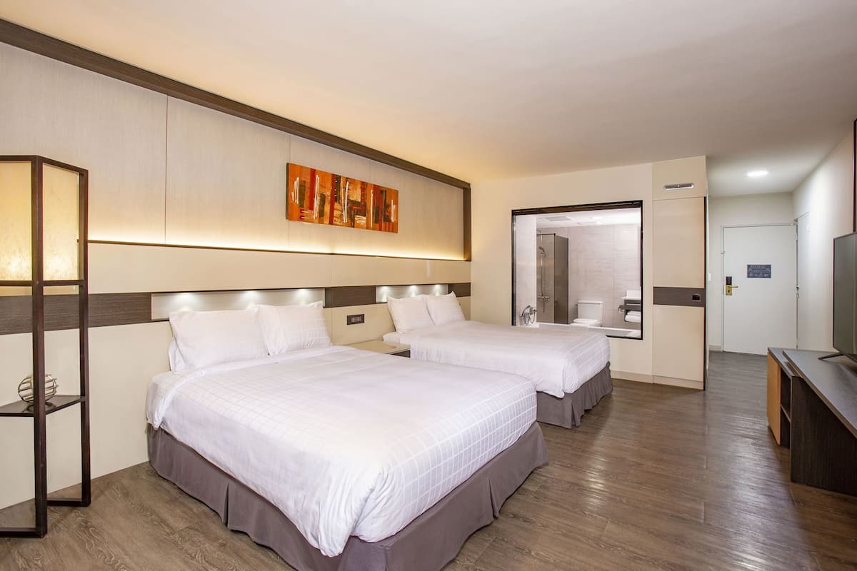 A hotel room with two beds, a large mirror, a television, and a wooden floor.