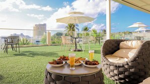 An outdoor dining area with a round table, chairs, and a wicker sofa. There are plates of food and drinks on the table. - Bayview Hotel Guam (Tamuning)