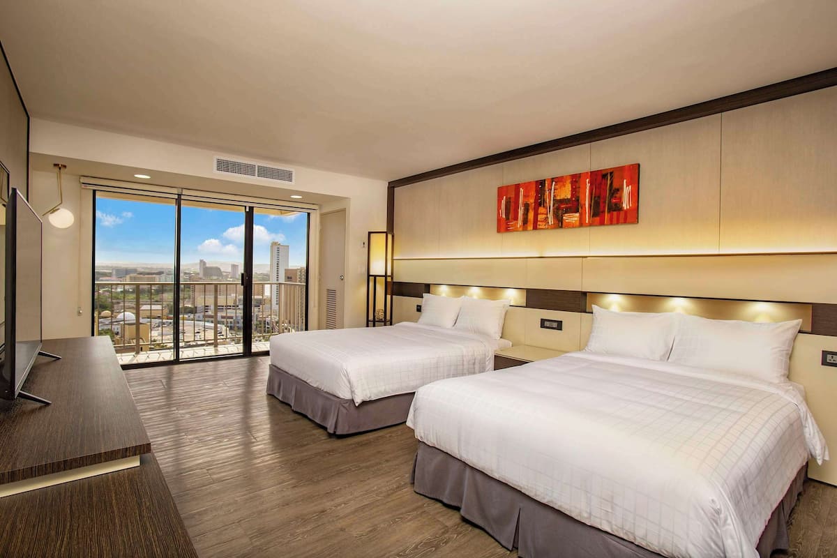 A hotel room with two beds, a desk, and a large window offering a city view.