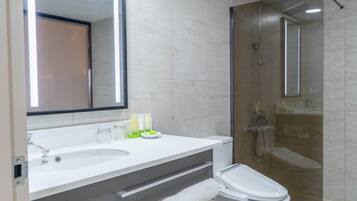 A modern bathroom with a large mirror, a sink, a toilet, and a glass-enclosed shower.