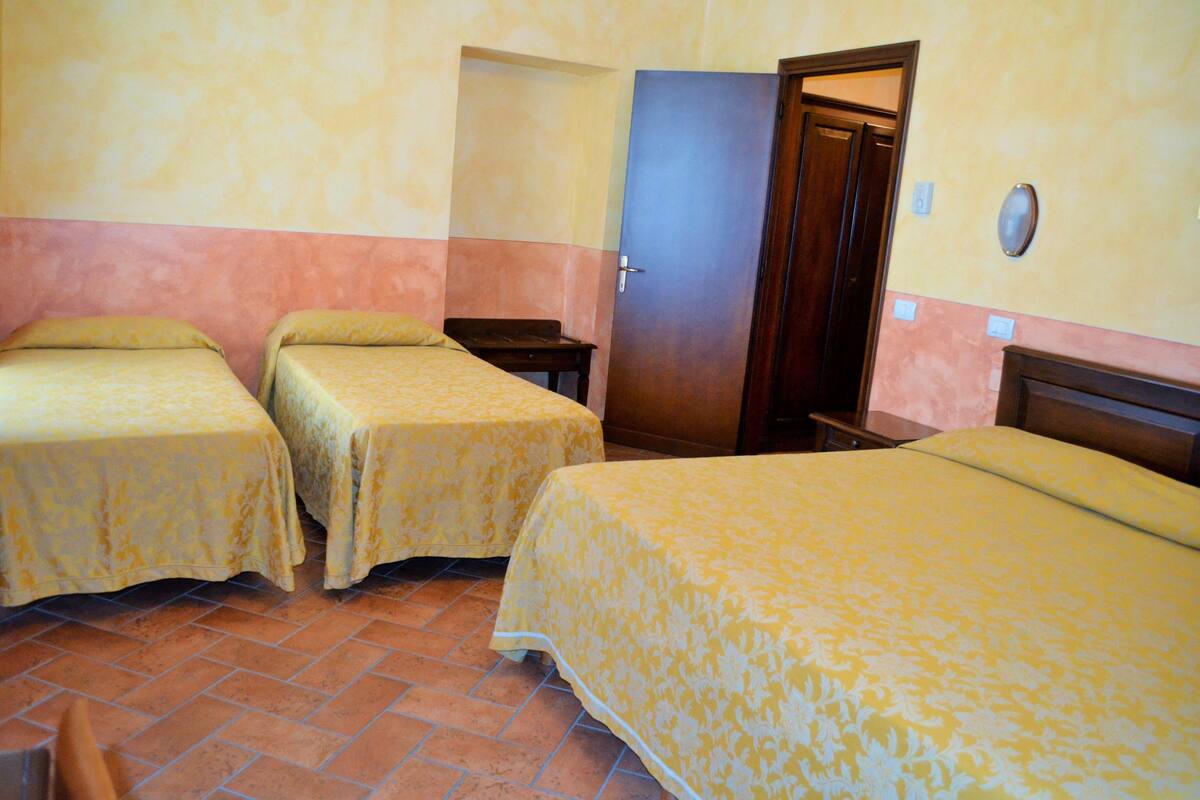 A room with three beds, a wooden door, and a tiled floor.