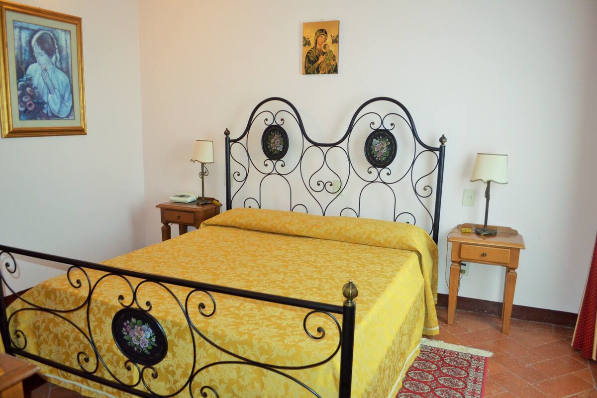 A neatly made bed with a yellow bedspread and a decorative headboard, two bedside tables with lamps, and a framed picture on the wall.