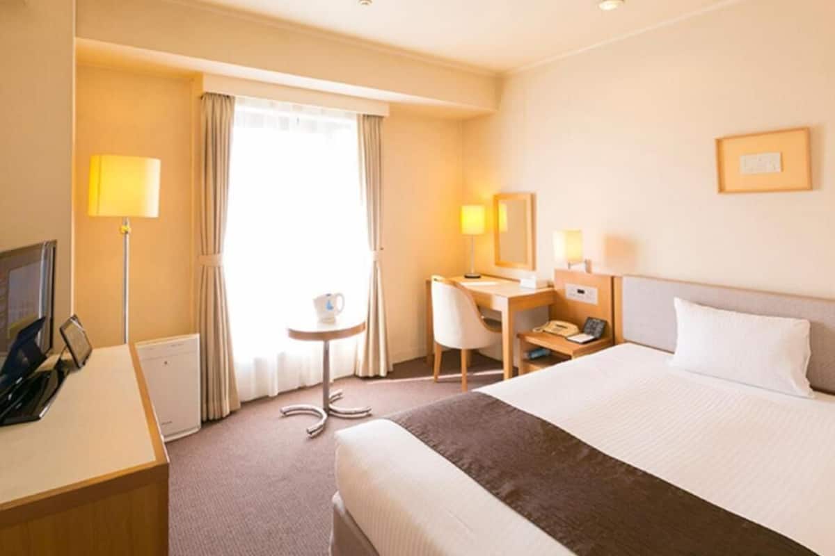 Een hotelkamer met een bed, bureau, stoel, lamp en een klein tafeltje met een kopje.