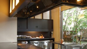 A modern kitchen with a long countertop, stainless steel appliances, and a view of a garden through a large window.