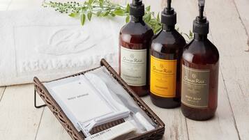 A wicker basket containing a body sponge, hair brush, and a toothbrush, alongside three bottles of orange rose body care products.
