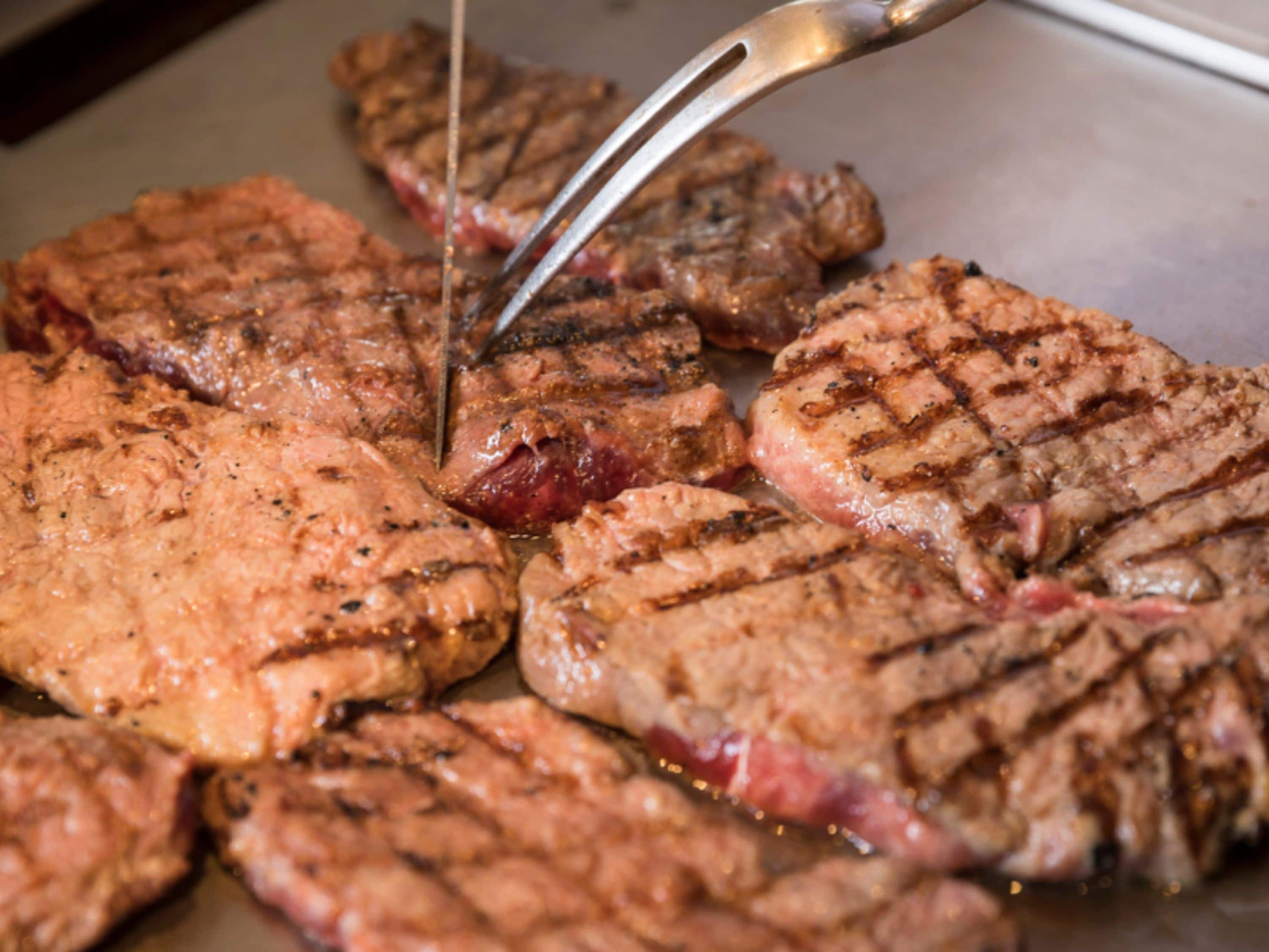 Grilled steaks on a tray with tongs.