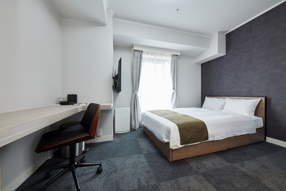 Een hotelkamer met een bed, een bureau, een stoel, een televisie en een raam met gordijnen.