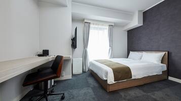 A hotel room with a bed, a desk, a chair, a TV, and a window with curtains.