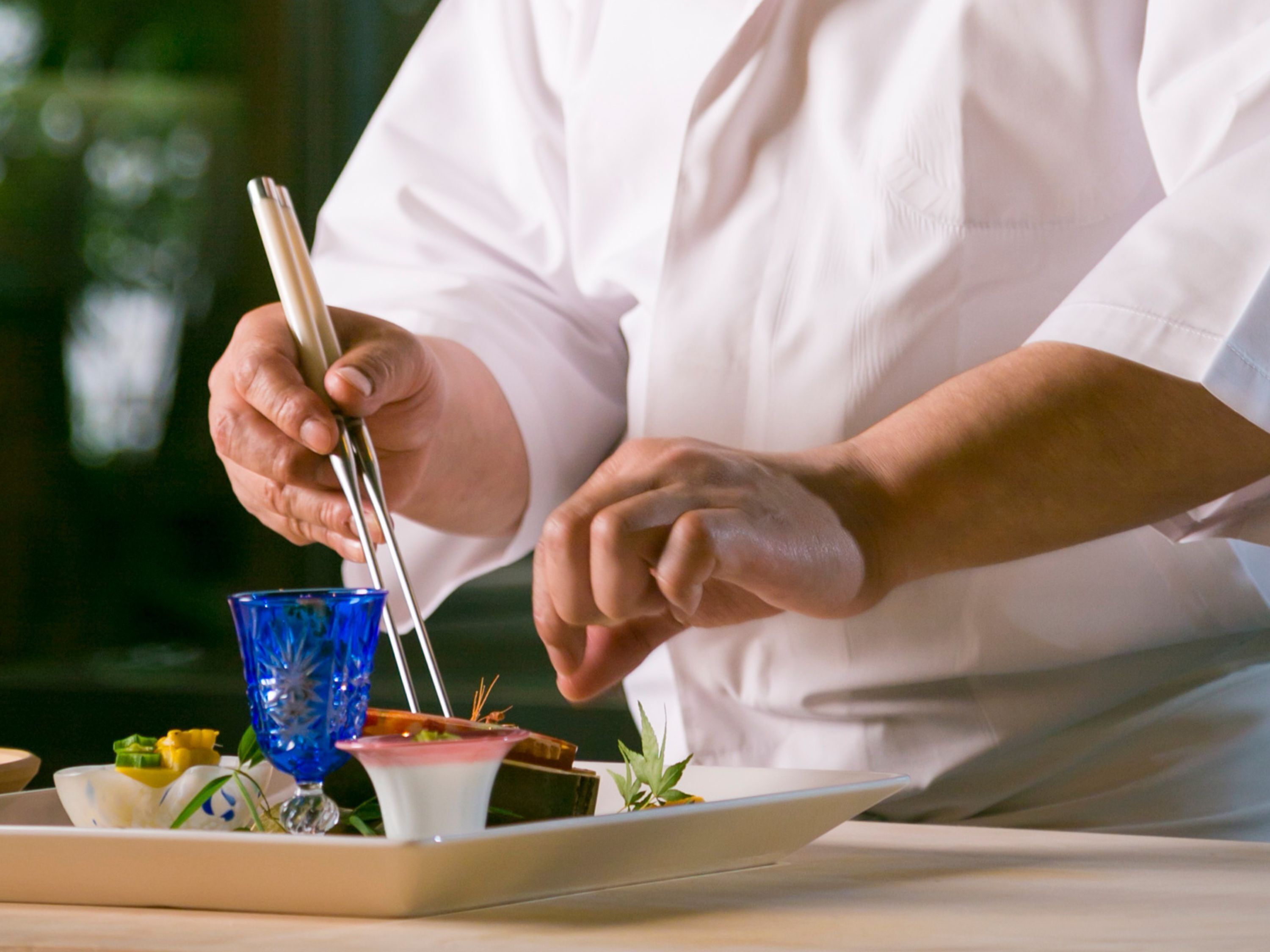 Una persona con camisa blanca preparando comida con palillos en un plato con varios platos.