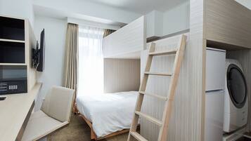 Habitación de hotel con cama, escritorio con silla, televisor, lavadora y ventana con cortinas.