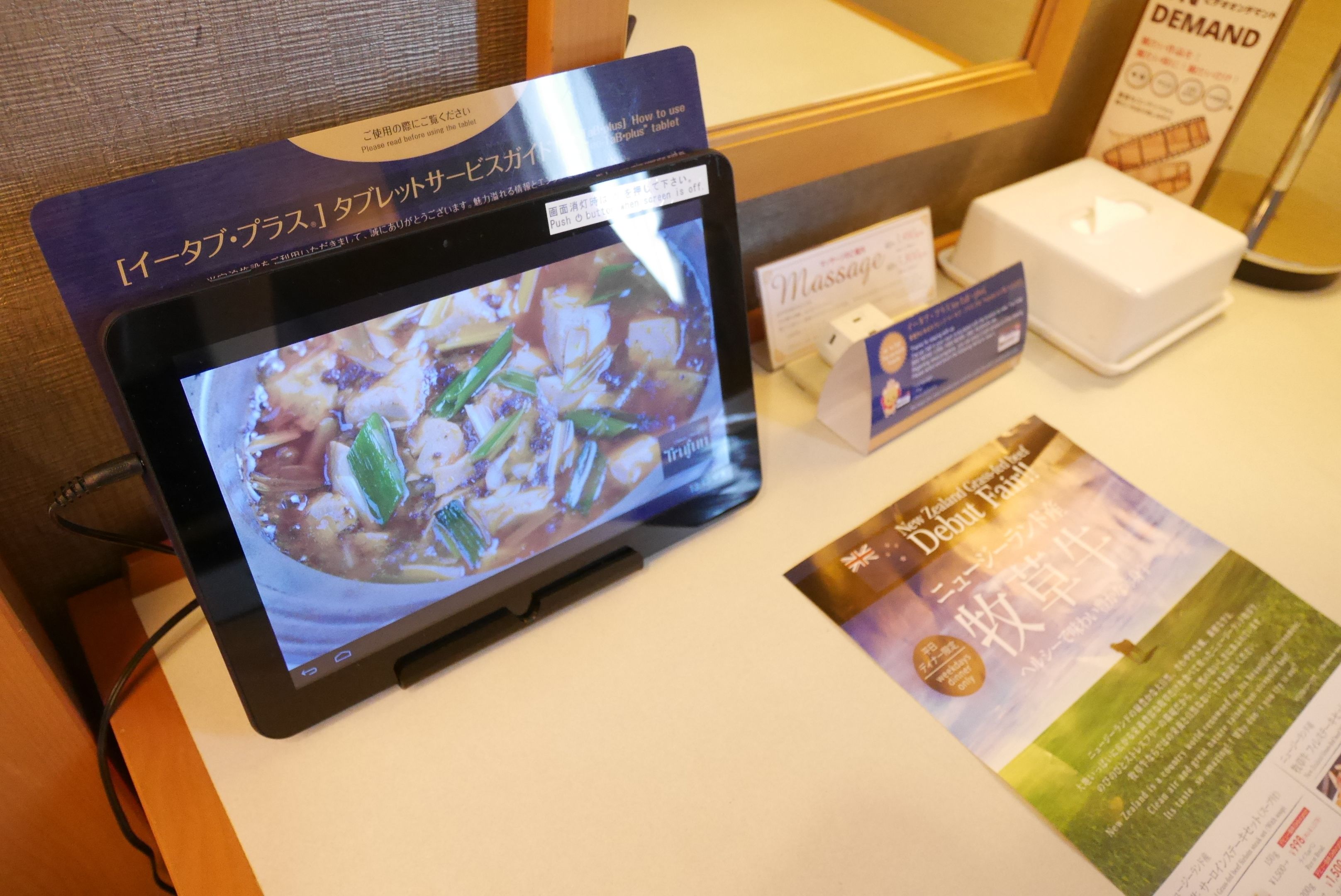 A tablet displaying a menu, a tissue box, and a brochure on a counter.