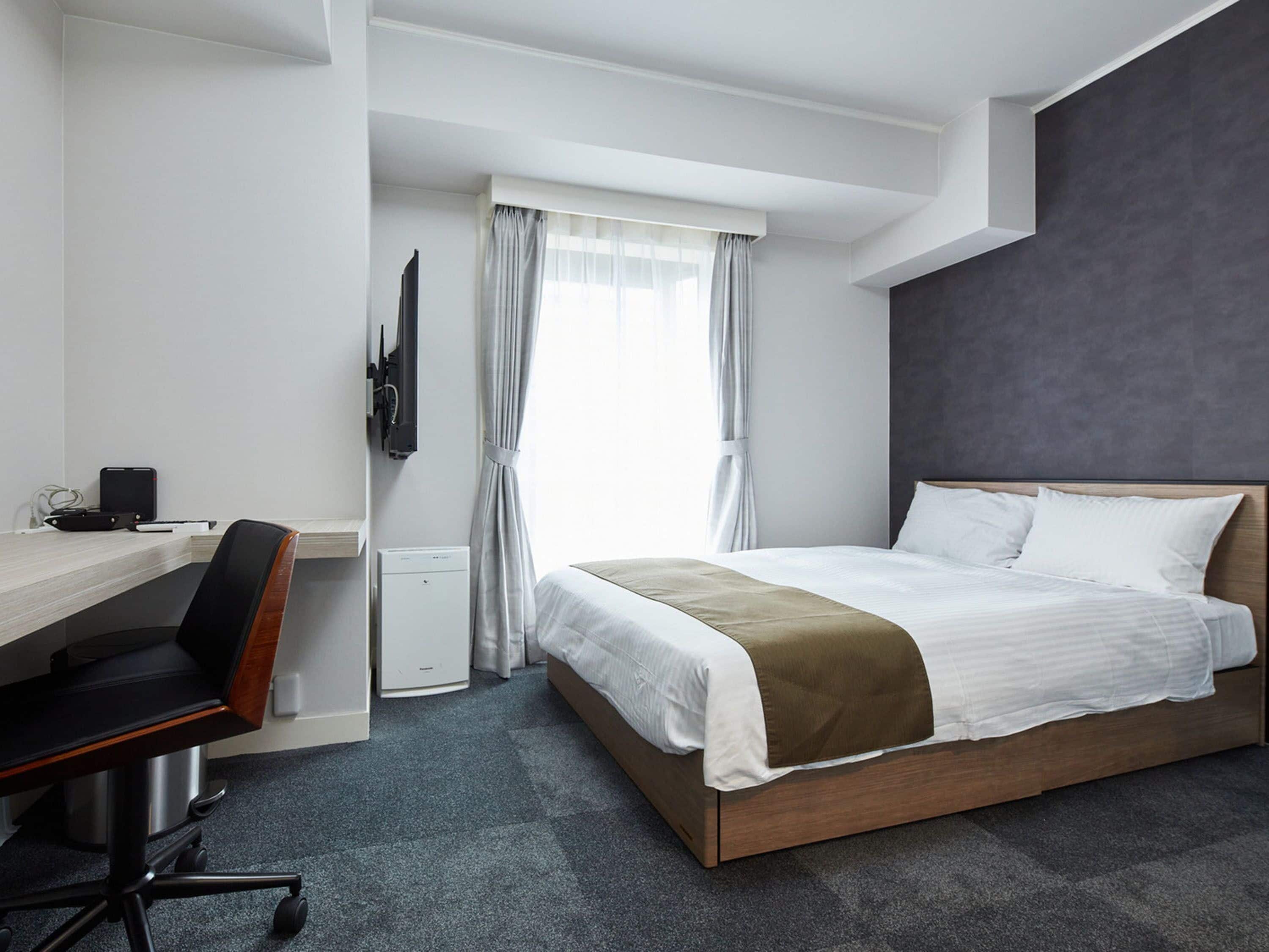 Quarto de hotel moderno com cama de madeira, escrivaninha com cadeira, televisão de tela plana e janela com cortinas.
