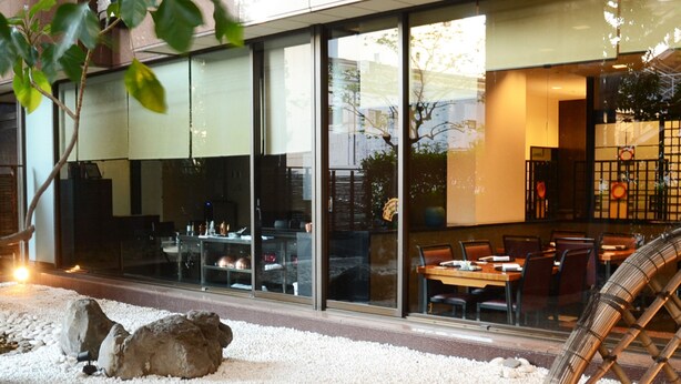 A restaurant with a glass facade, outdoor seating, and a small water feature.
