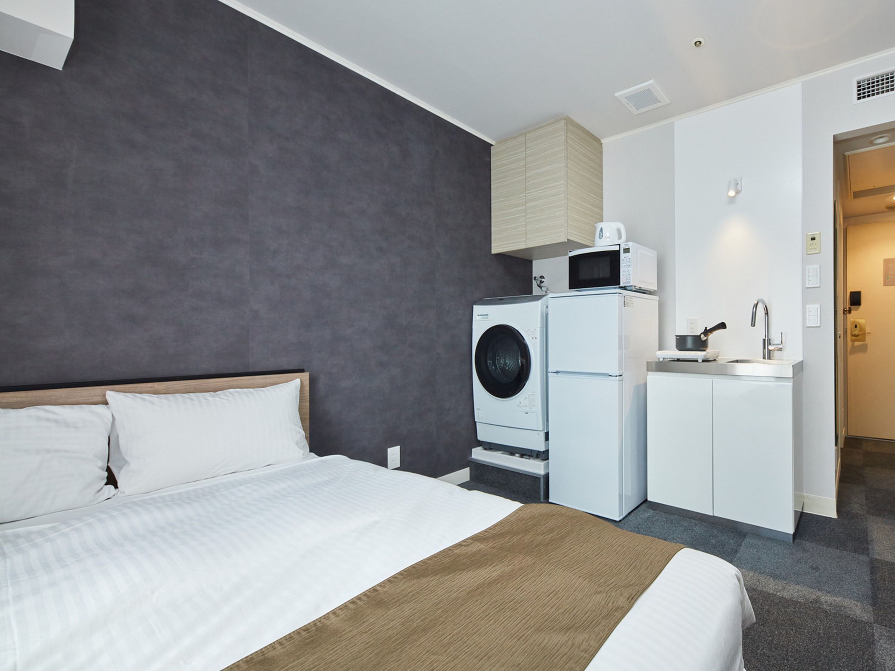 Hotellihuone, jossa on sänky, pesukone, mikroaaltouuni ja pesuallas.