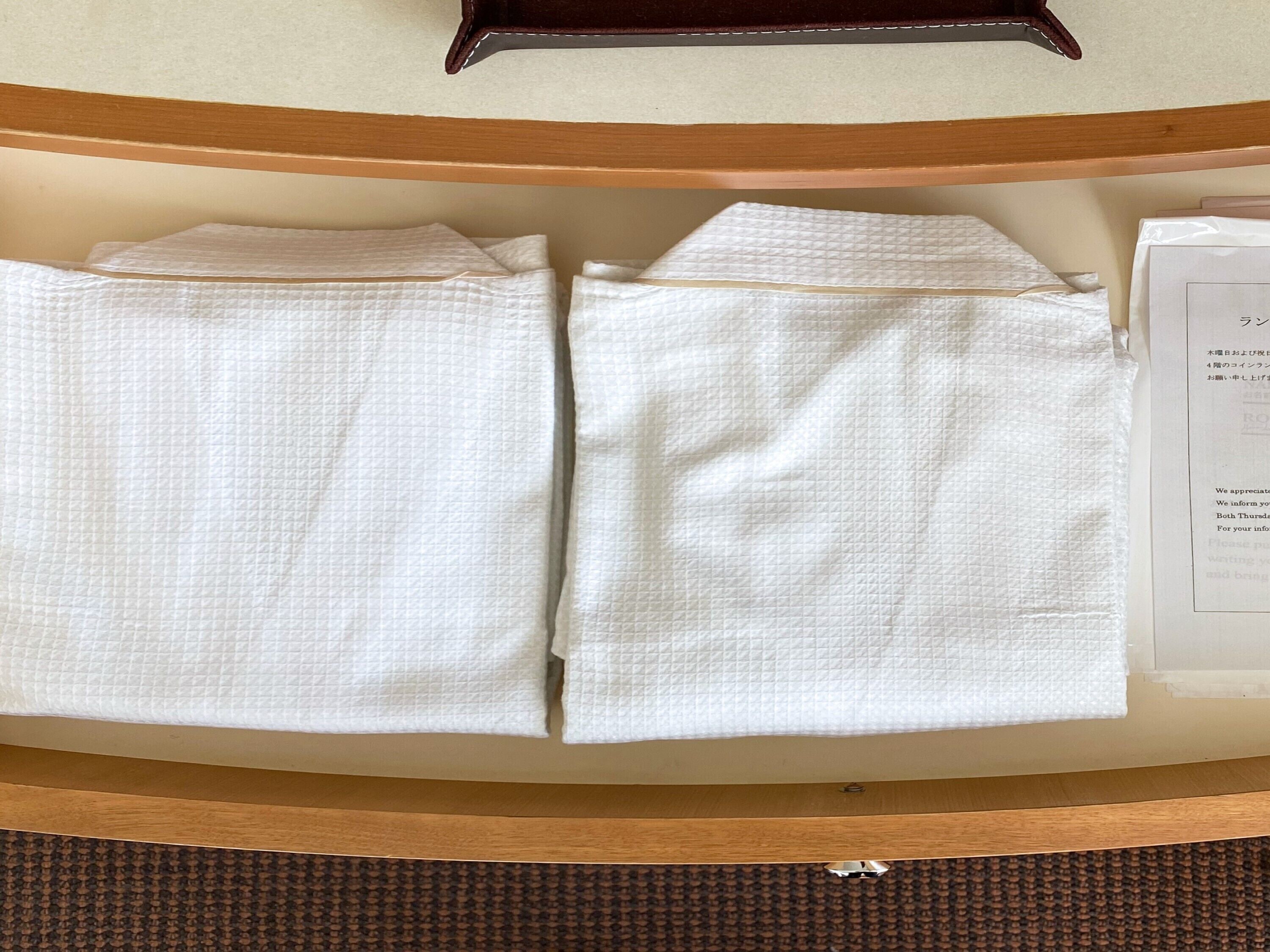 A neatly arranged set of white towels on a wooden shelf in a hotel room.