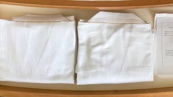 A neatly arranged set of white towels on a wooden shelf in a hotel room.