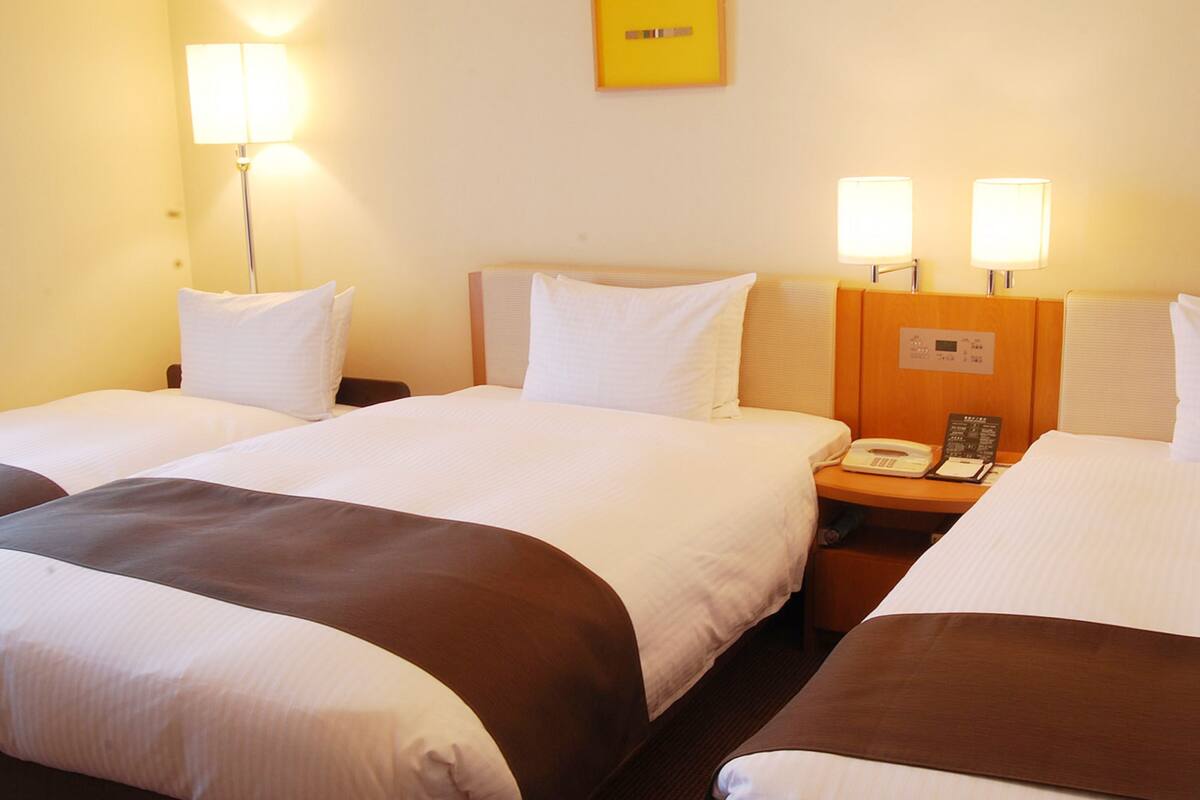 Een hotelkamer met twee bedden, elk voorzien van een kussen en een deken. Er is een nachtkastje met een telefoon en een klein tafeltje.