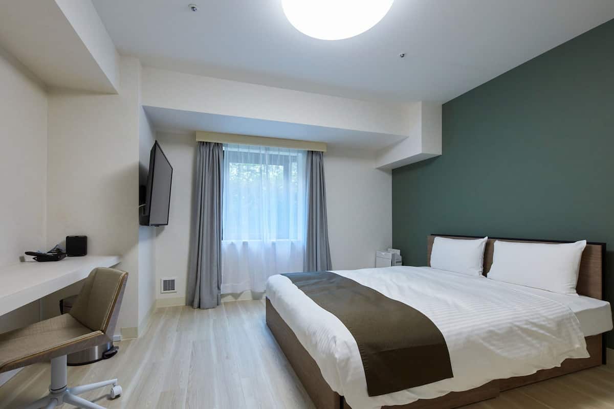 Een moderne hotelkamer met een groot bed, een bureau met stoel, een flatscreen-televisie en een raam met gordijnen.