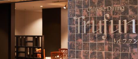 Interior de un restaurante con una pared de azulejos que muestra el nombre 'Chinese Dining Trifun'.