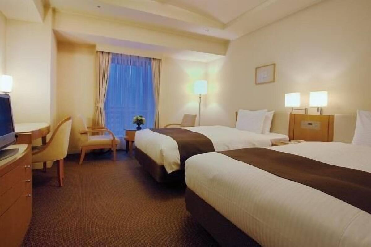 Een hotelkamer met twee bedden, een bureau, een stoel en een televisie.