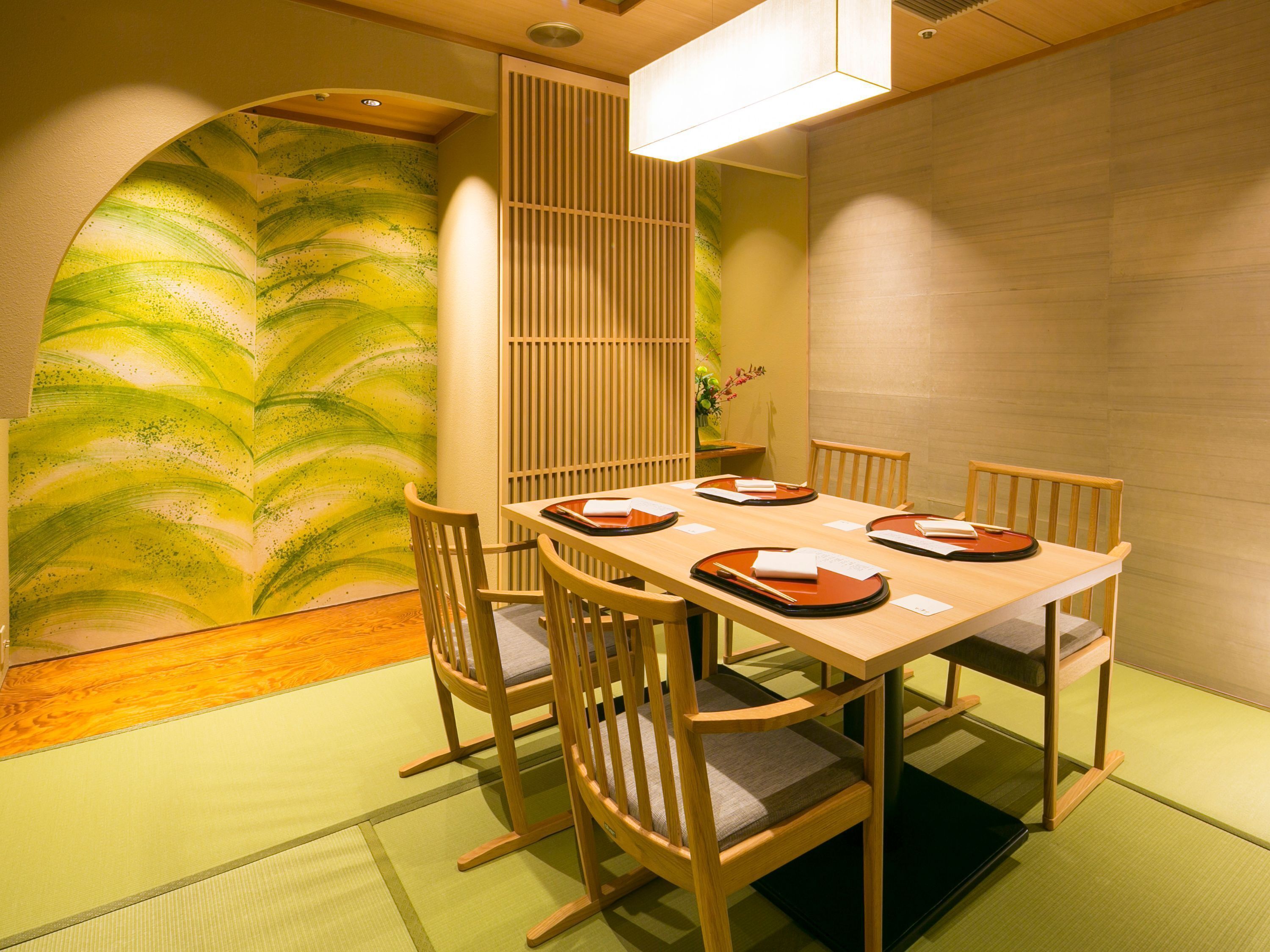 A traditional Japanese dining room with tatami flooring, a low table, wooden chairs, and a shoji screen.