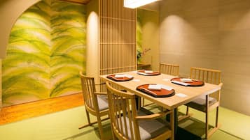 A traditional Japanese dining room with tatami flooring, a low table, wooden chairs, and a shoji screen.