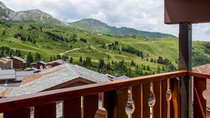 A mountain view from a balcony with wooden railings, a winding road, and buildings with traditional architecture.