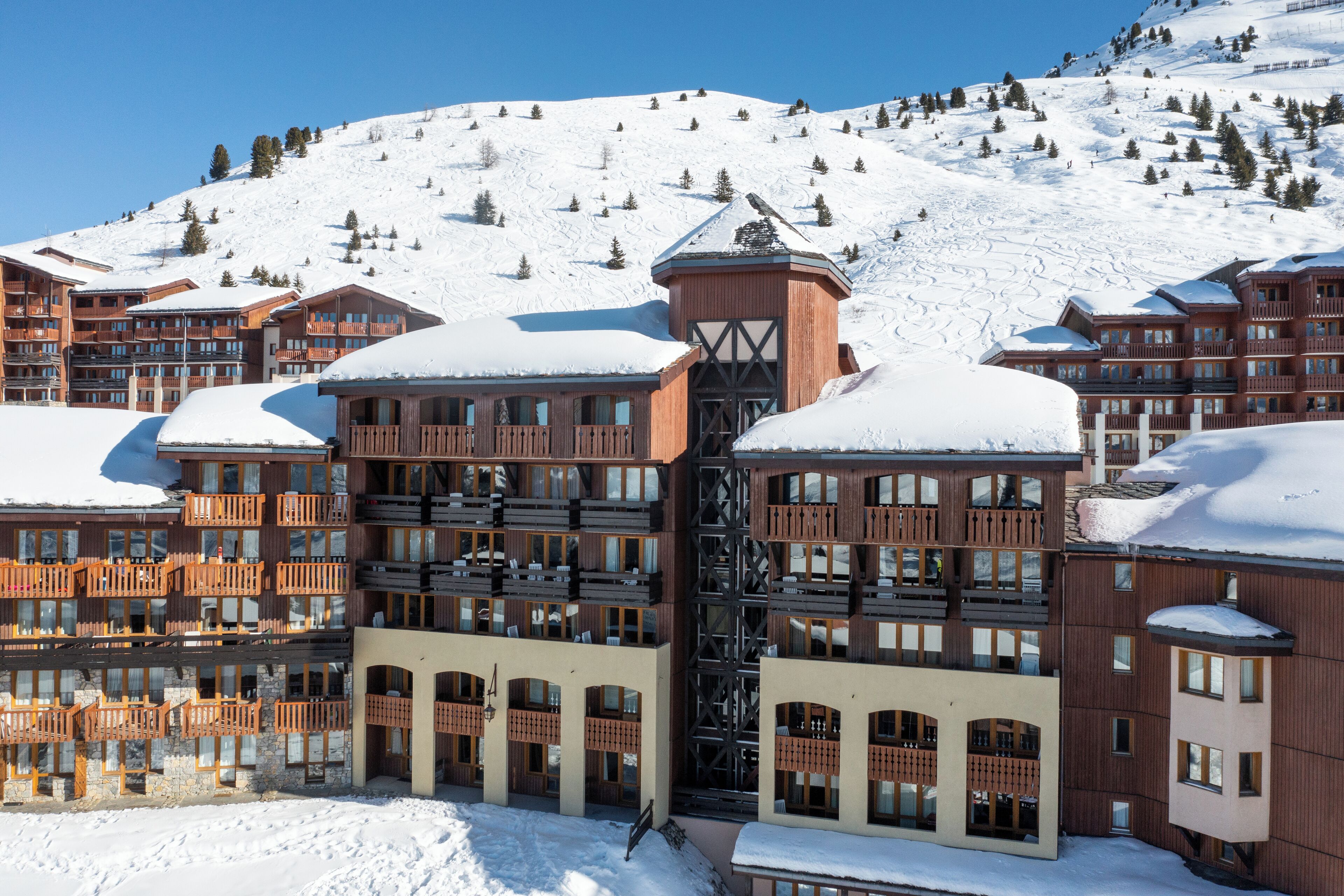 Un hôtel à plusieurs étages, doté de balcons, avec une piste de ski en arrière-plan.