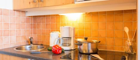 A kitchen with wooden cabinets, a microwave, a coffee maker, a pot, a red pepper, and a knife on the counter.