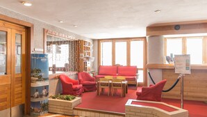 A hotel lobby with a red carpet, red sofas, a wooden reception desk, and a blue refrigerator.