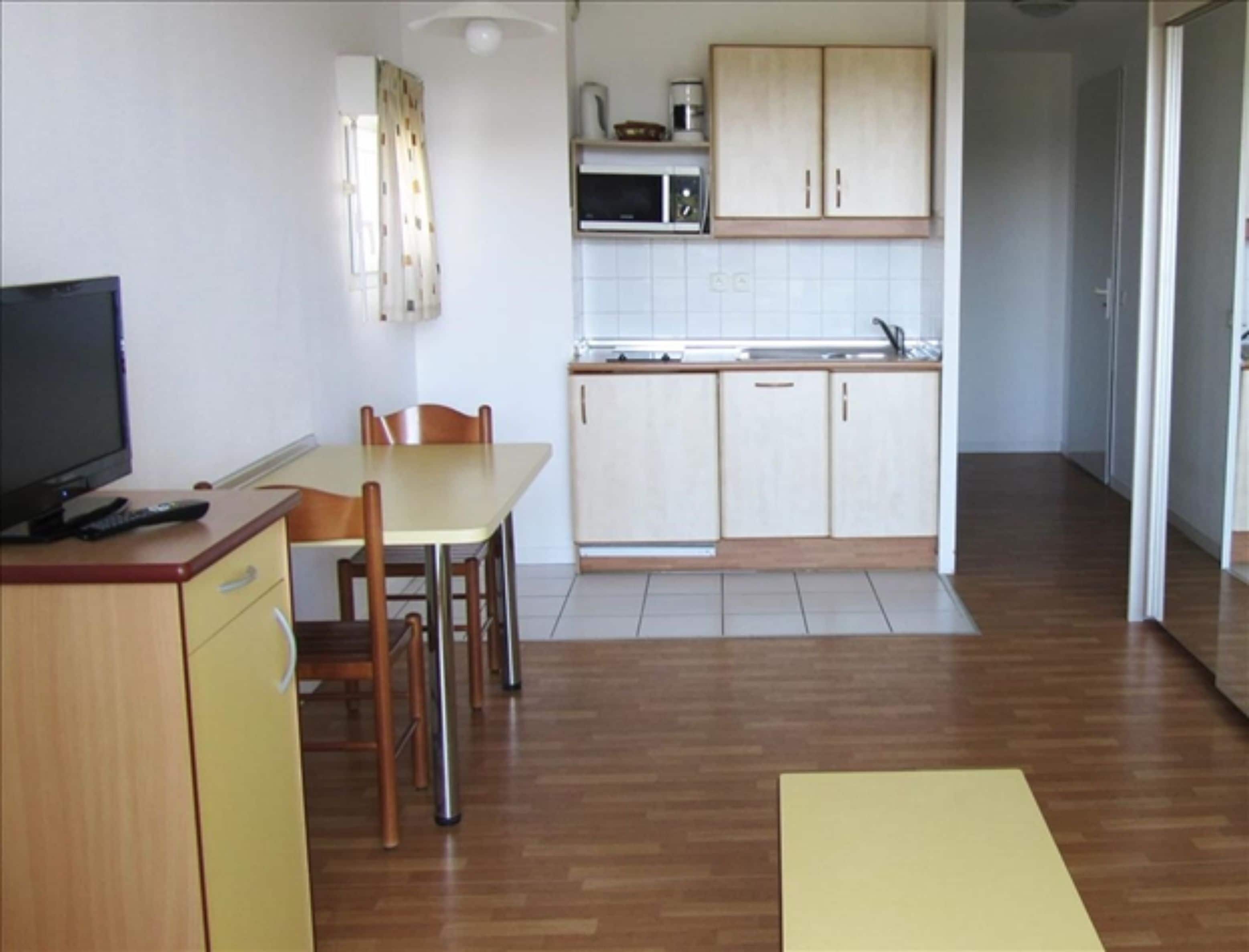 A compact kitchen with a dining area, a microwave, and a television on a wooden cabinet.