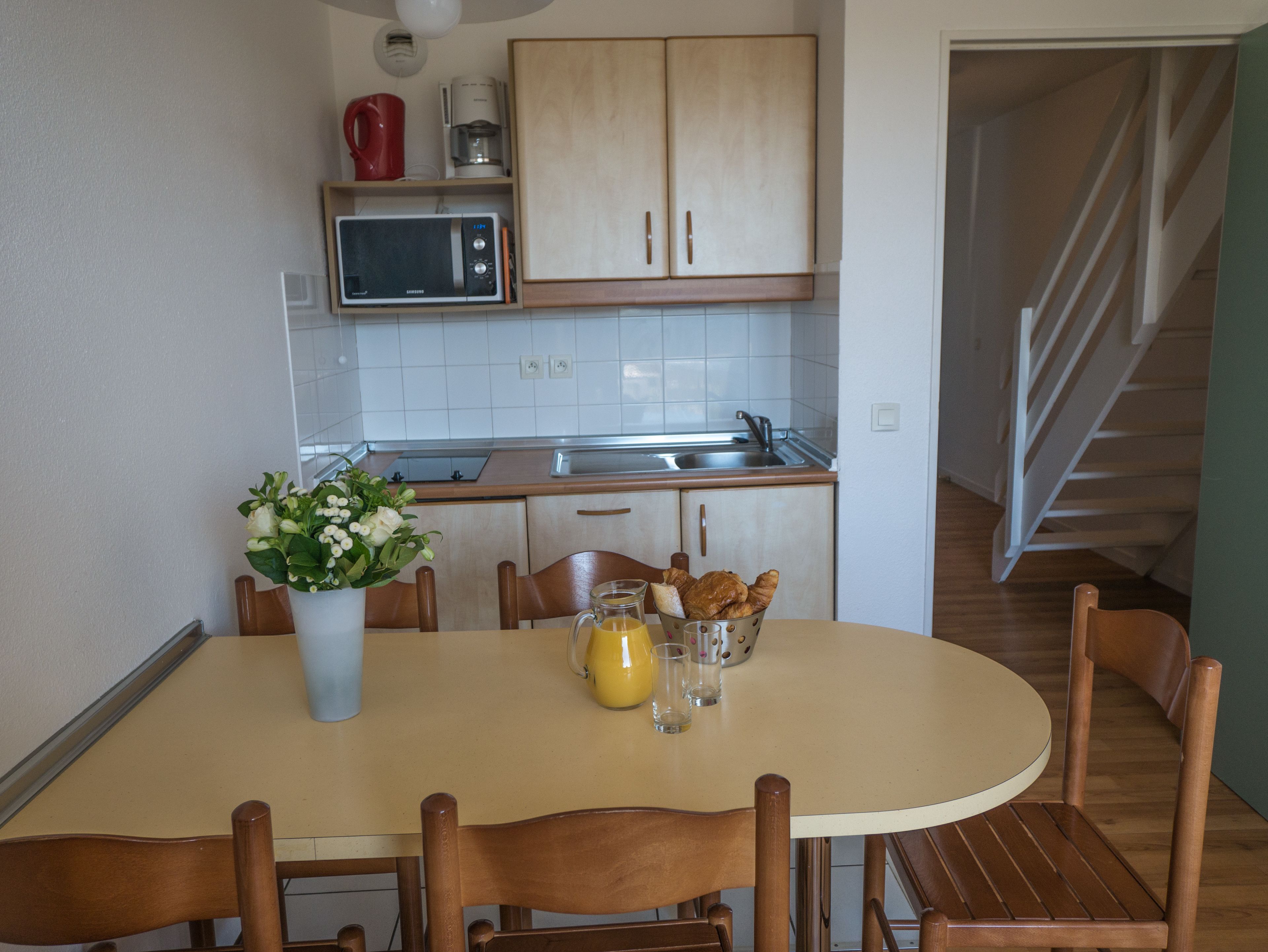 A kitchen with wooden cabinets, a microwave, a coffee maker, and a dining table with chairs.